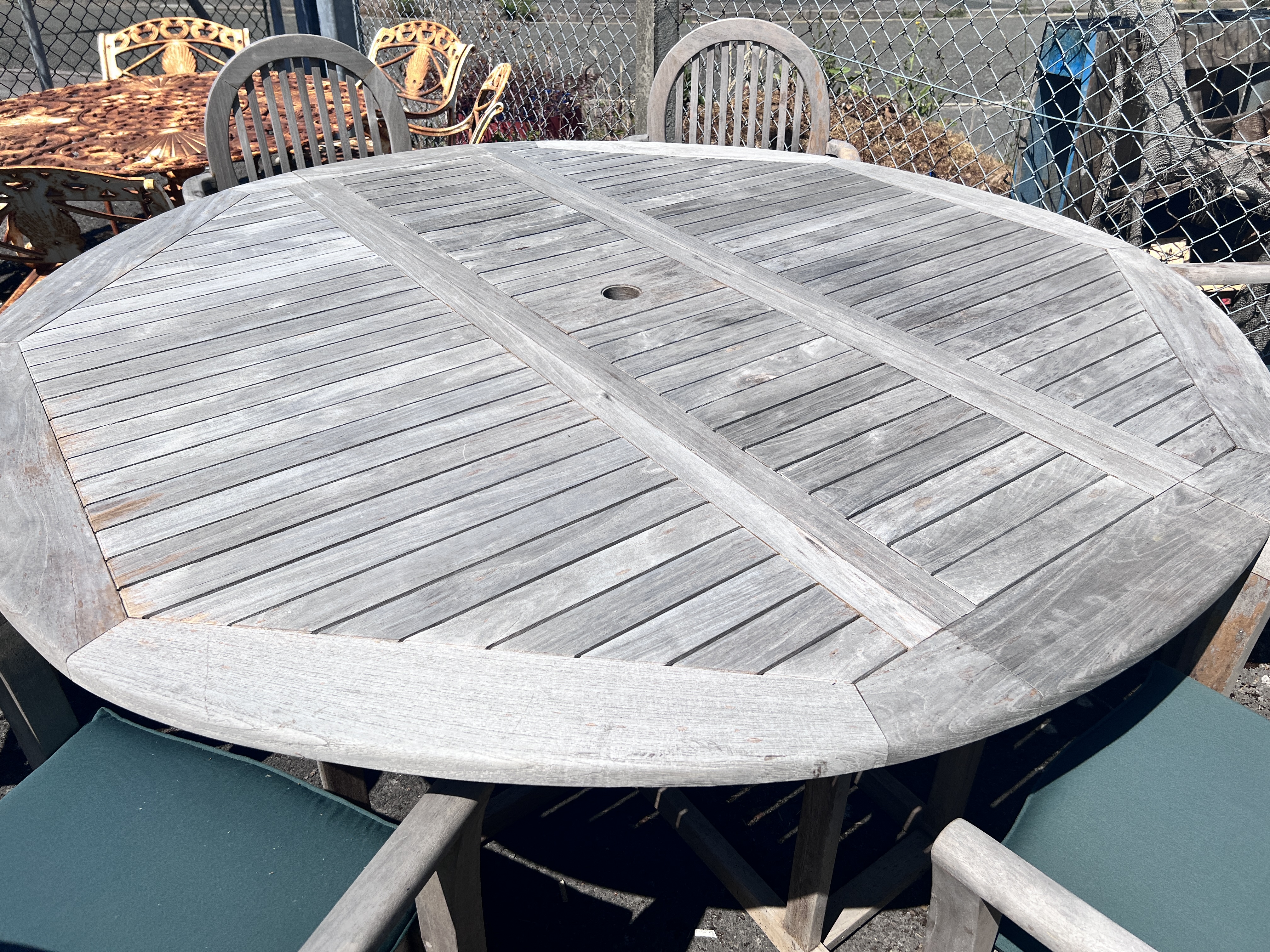 A circular weathered teak drop leaf garden table, 180cm extended, height 78cm, and six elbow chairs with seat cushions